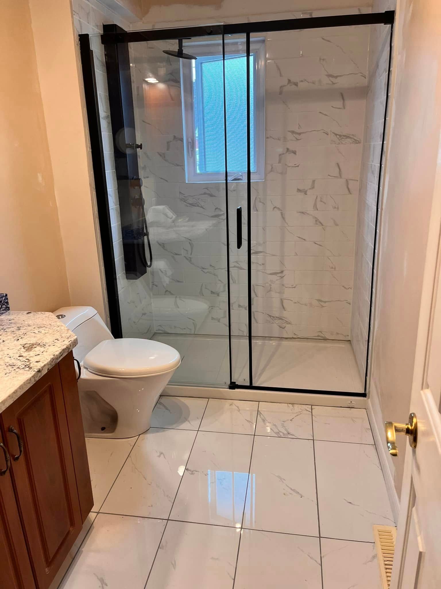 Une salle de bains moderne avec sols et murs de douche carrelés à motif marbre blanc, comprenant une douche en verre et des toilettes blanches.