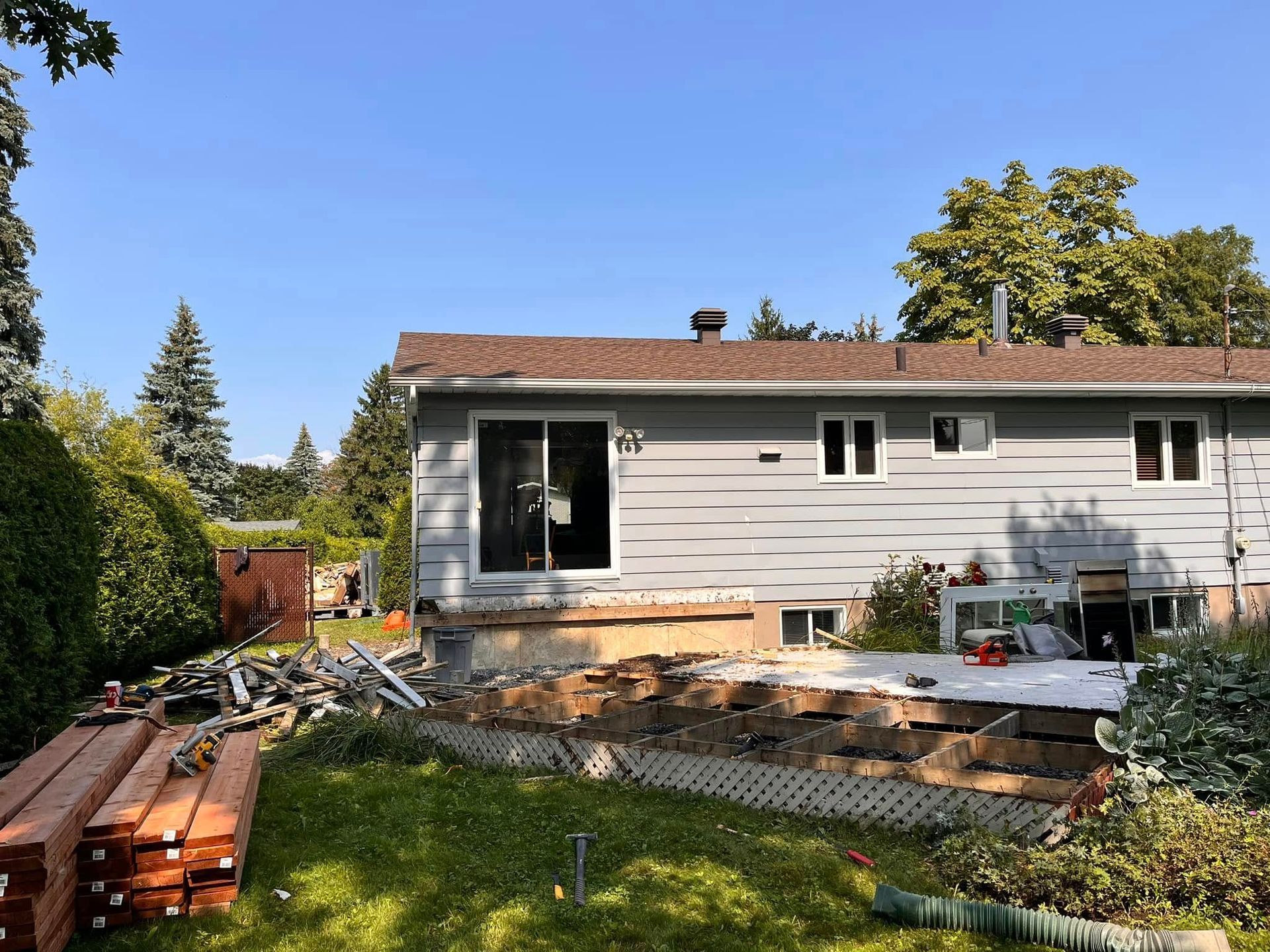 Extérieur d'une maison avec un mur gris et une terrasse en bois partiellement démolie dans la cour arrière.