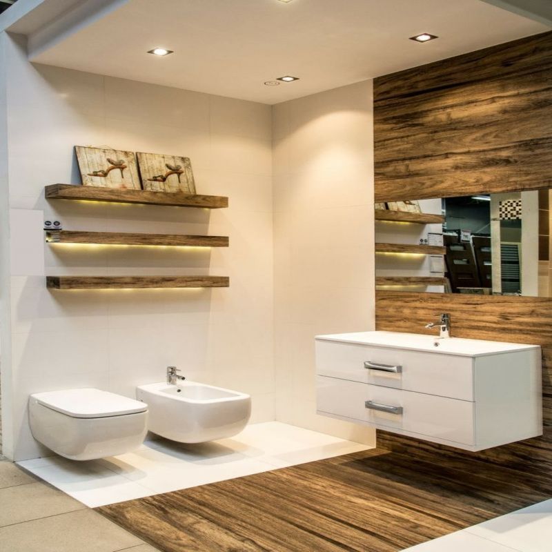 Une salle de bains moderne aménagée avec des accessoires muraux blancs, des éléments en bois, des étagères éclairées et un sol en bois.
