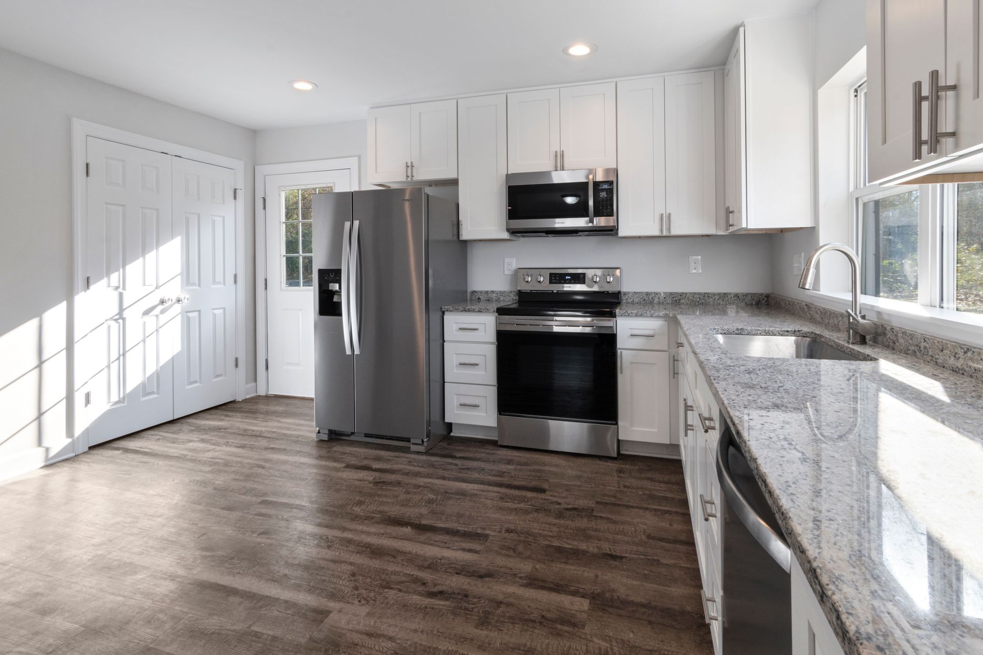 Cuisine moderne et lumineuse avec armoires blanches, électroménagers en acier inoxydable, comptoirs en granit et plancher en bois.