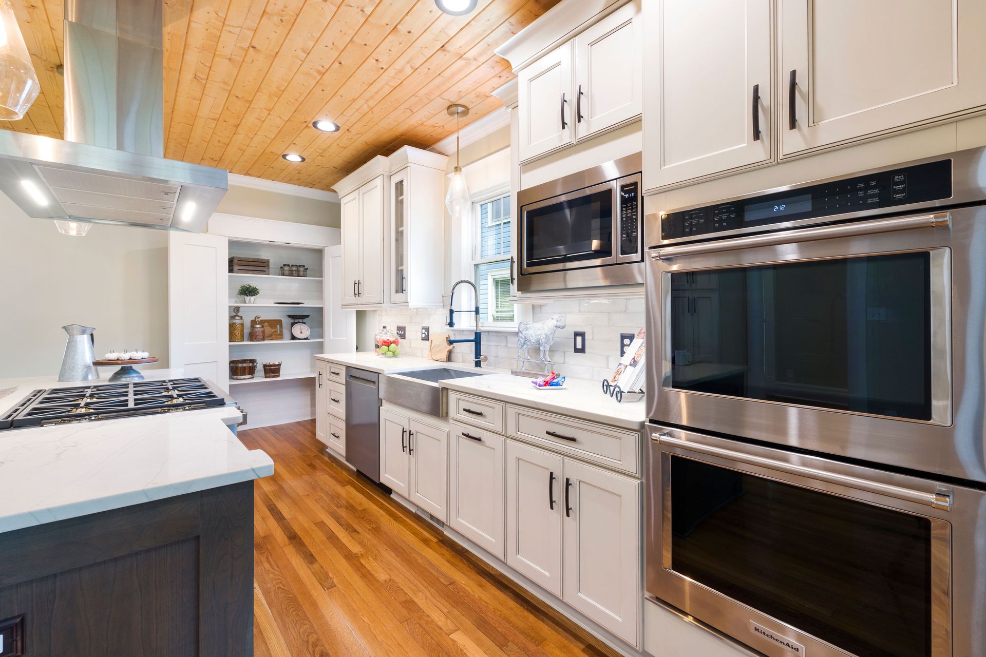 Cuisine moderne et lumineuse avec placards blancs, électroménager en inox et parquet au plafond et au sol.