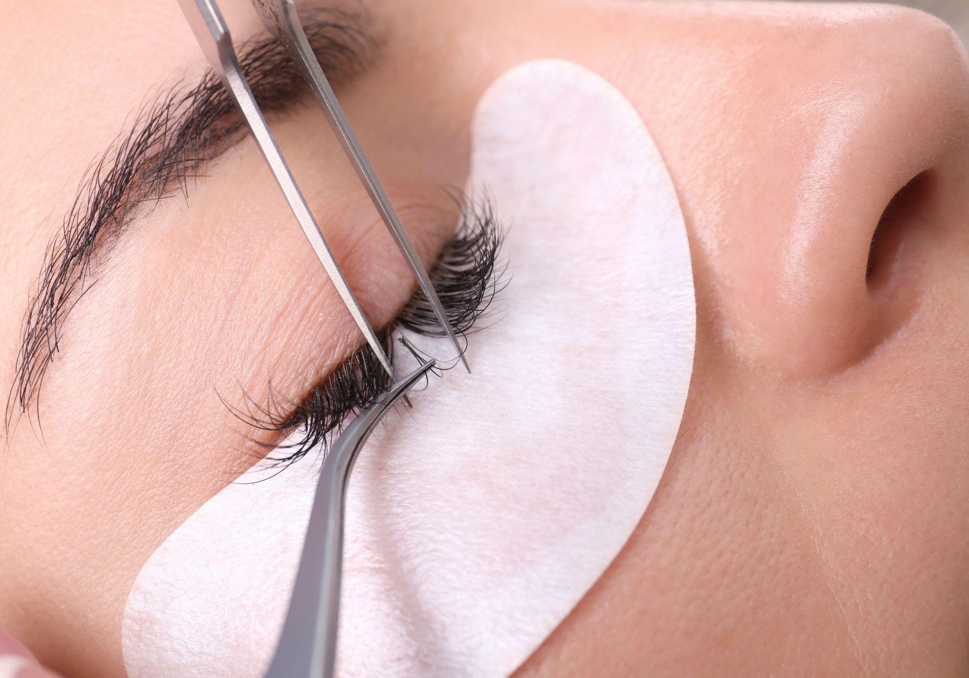 Eyelash extension being applied to a closed eye with white under-eye pads
