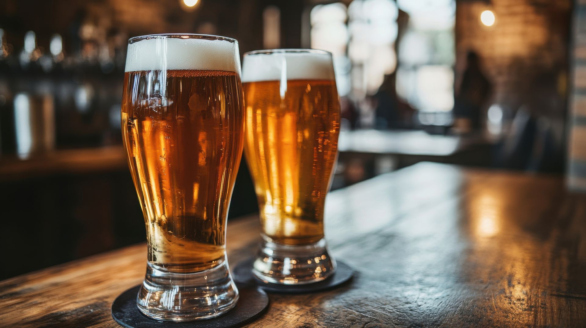 Two glasses of beer are sitting on a wooden bar.