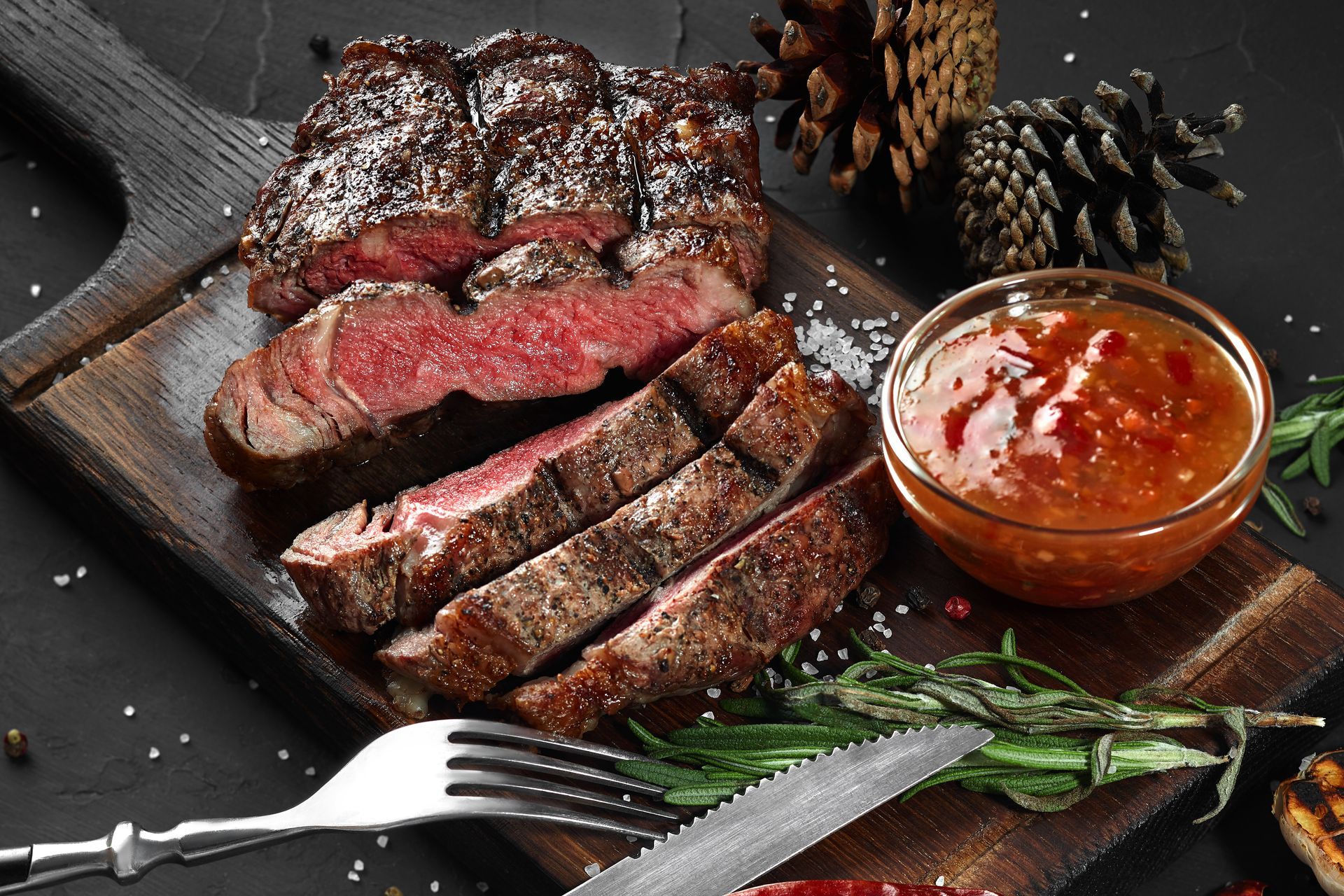 A steak is sitting on a wooden cutting board next to a bowl of sauce.