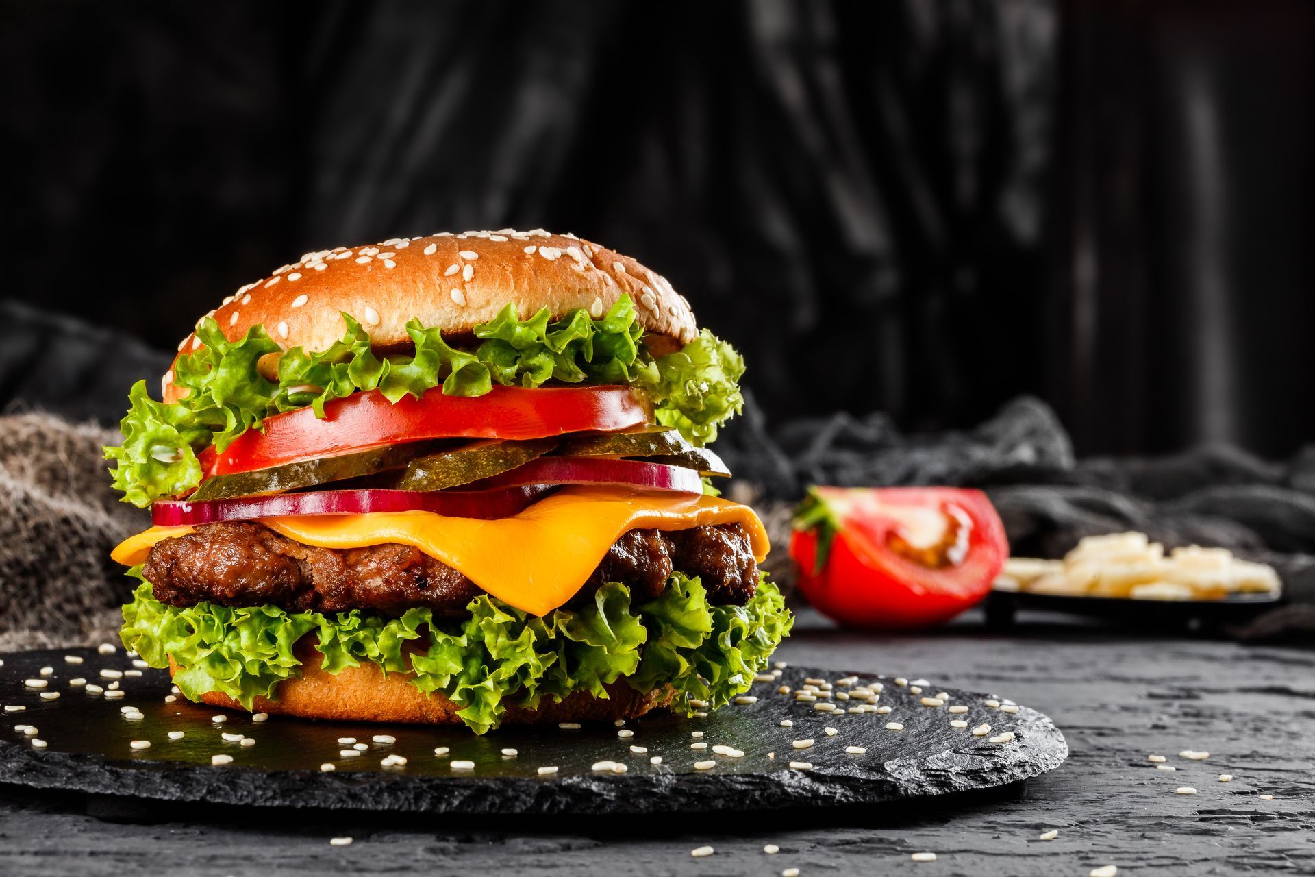 A hamburger with lettuce , tomatoes , pickles and cheese on a black plate.