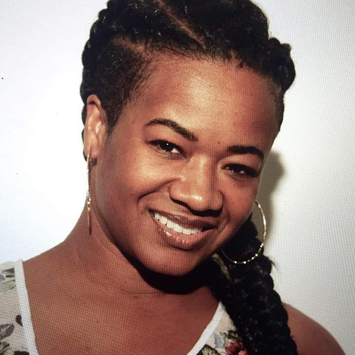 A woman with braids and hoop earrings smiles for the camera