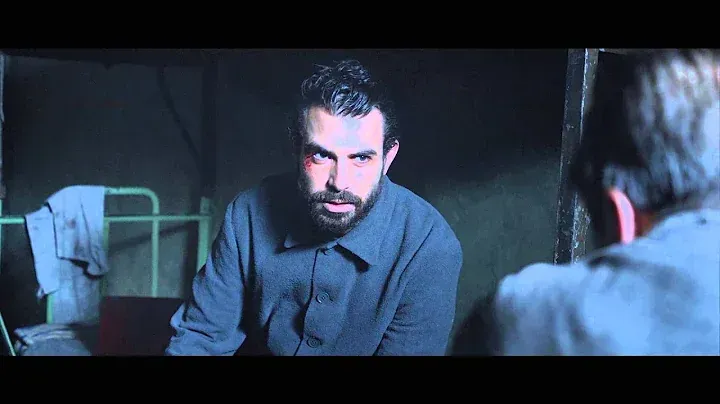 A man with a beard is sitting in a dark room talking to another man.