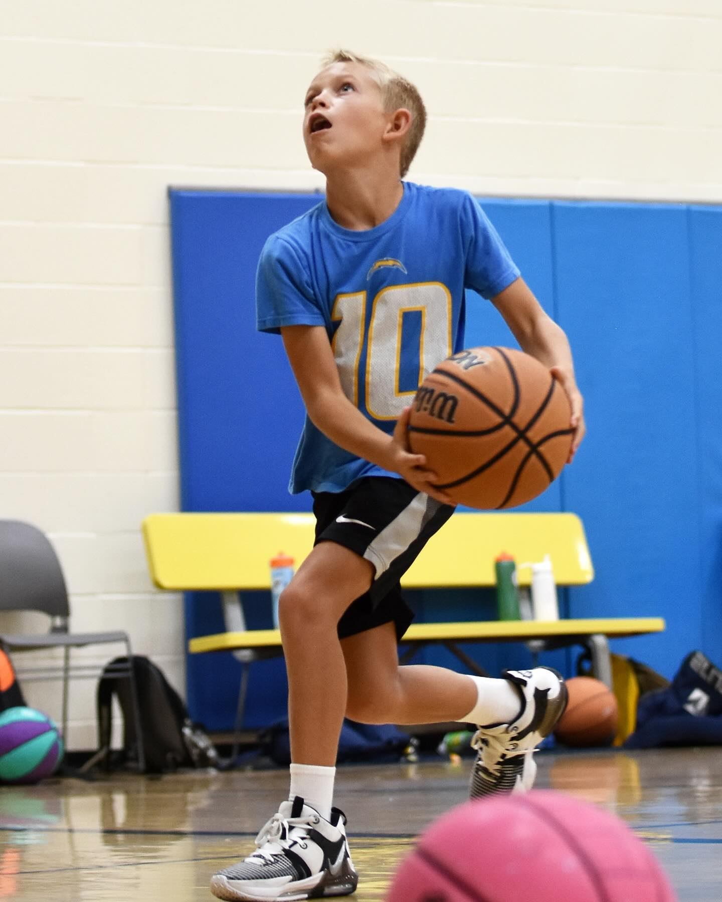 Basketball player in white and yellow shoots a pink ball in a gymnasium