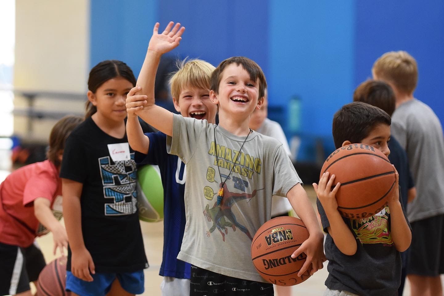 Boy reaching for a basketball during an indoor gym practice, with other players in the background