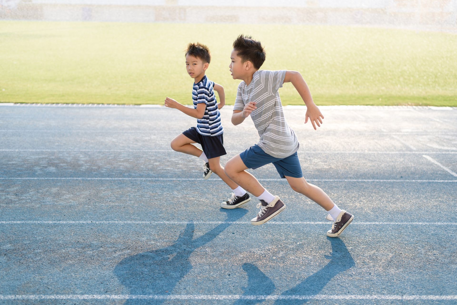 Two children sprinting on a blue track, with a green field in the background.