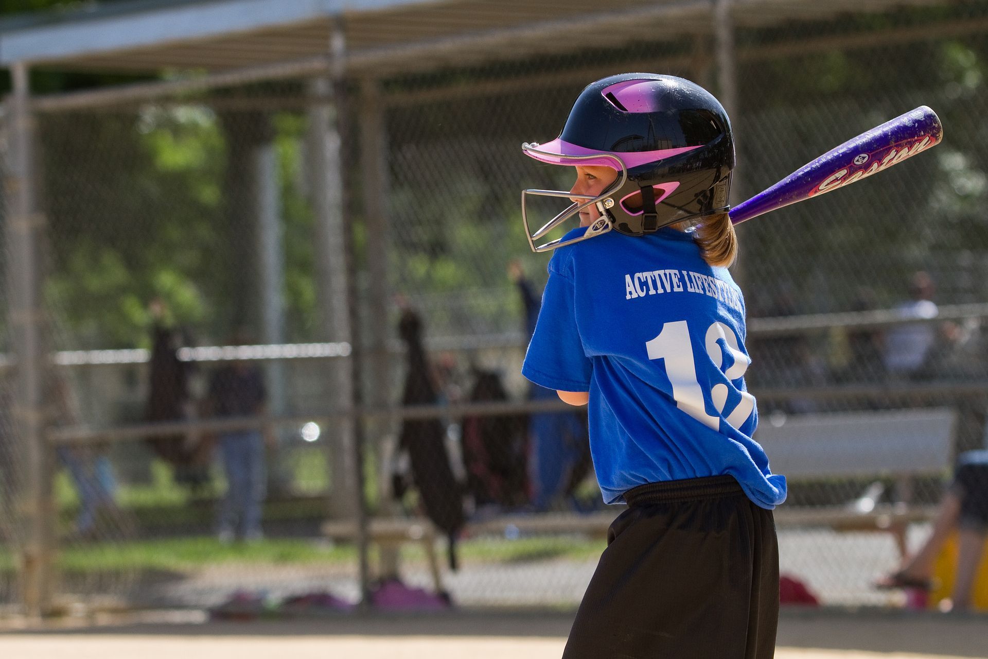Young softball player in blue jersey and pink helmet swinging a bat at home plate