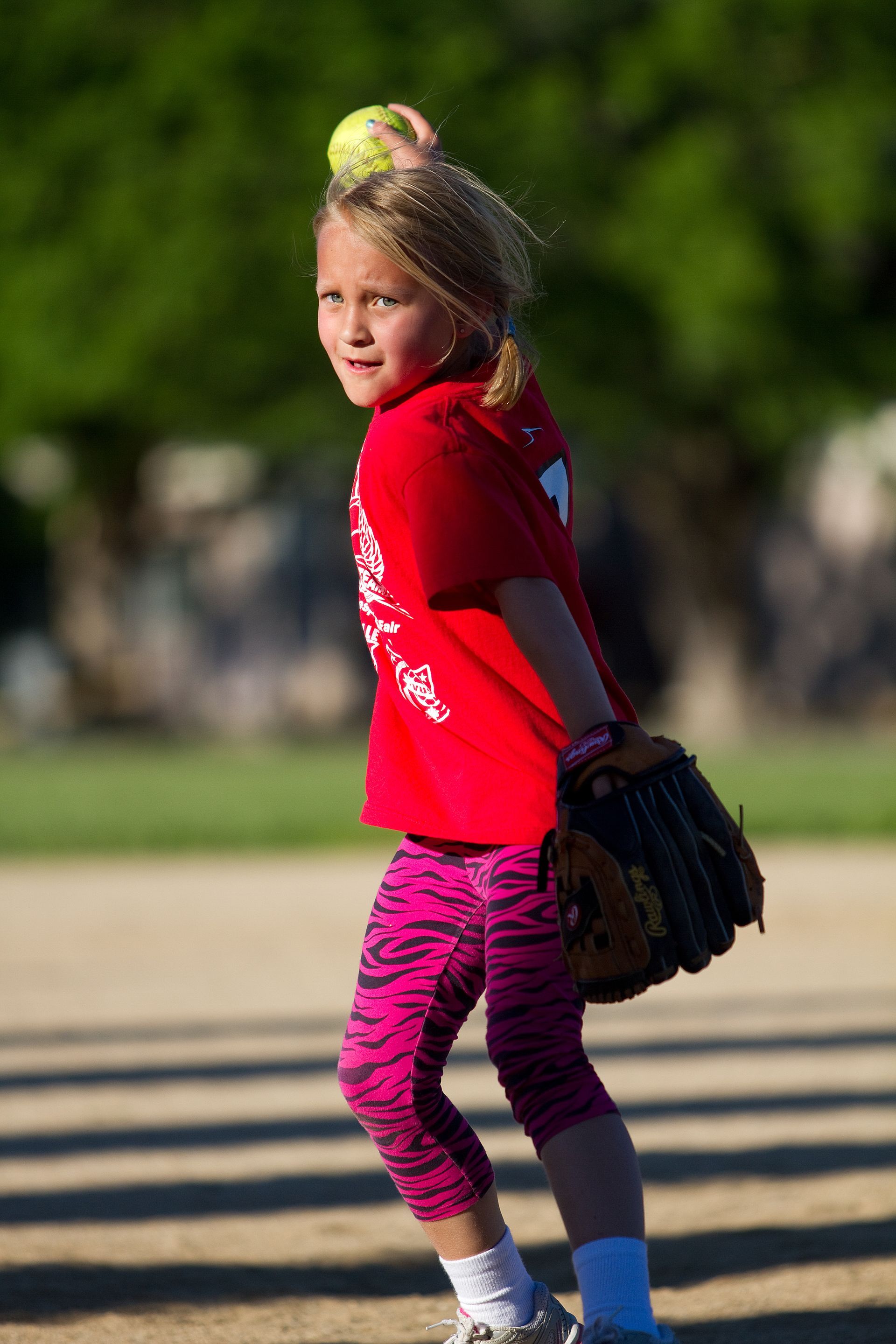 Child in red shirt and pink leggings holding a baseball glove on a field