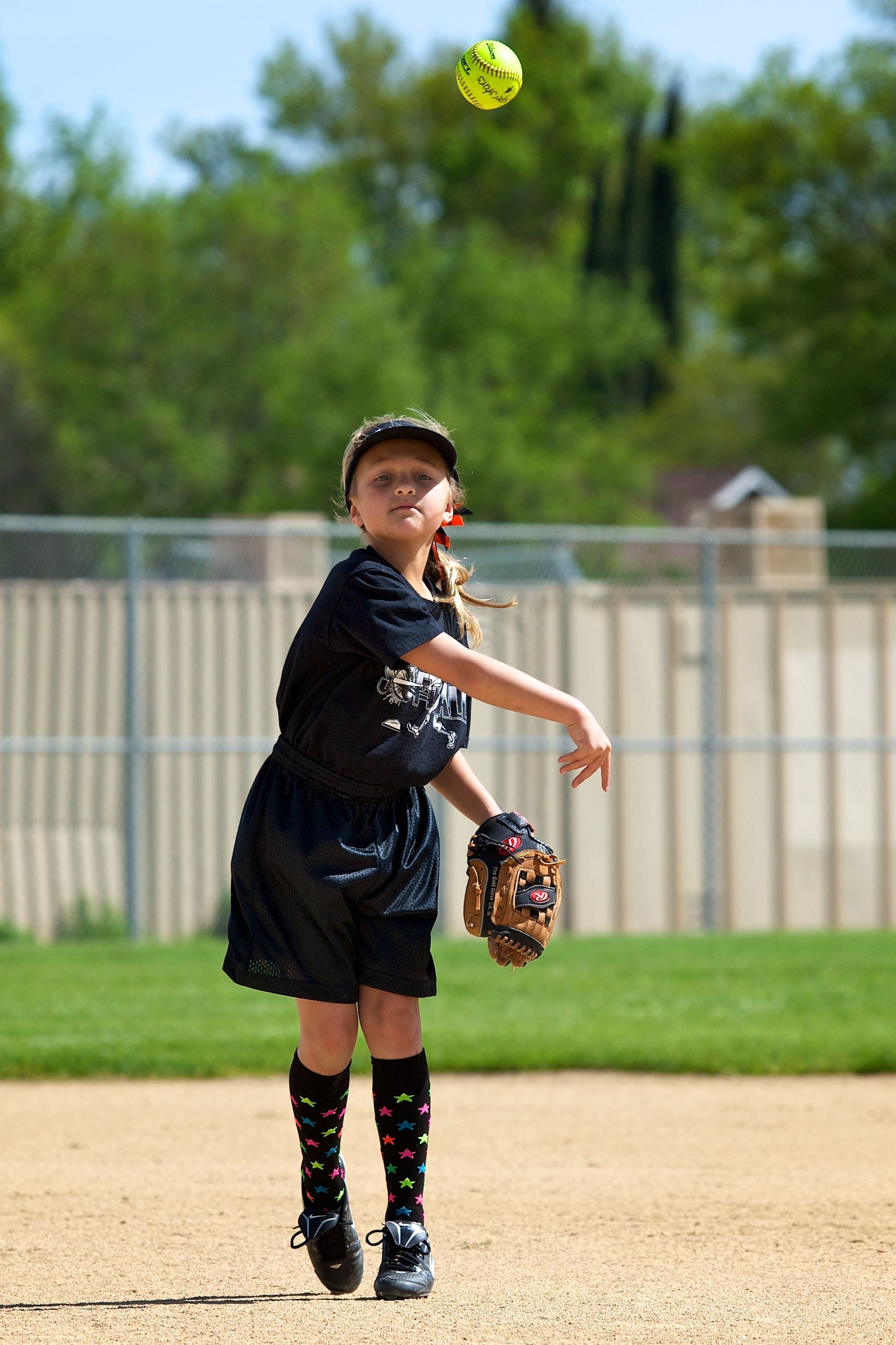 Softball player catching a bright yellow ball on a dirt field, with a glove in hand.