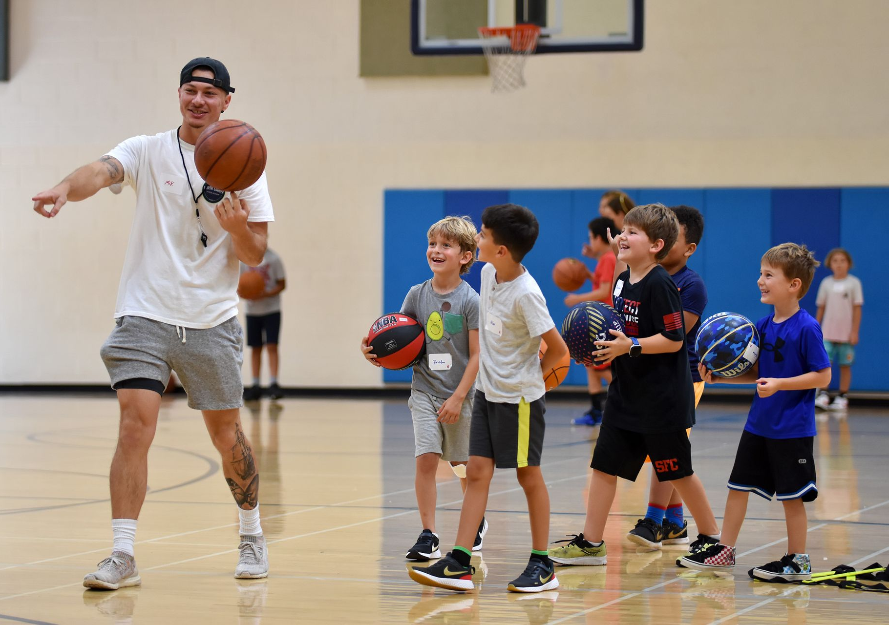 Coach dribbling a basketball beside a line of kids in a gym during practice