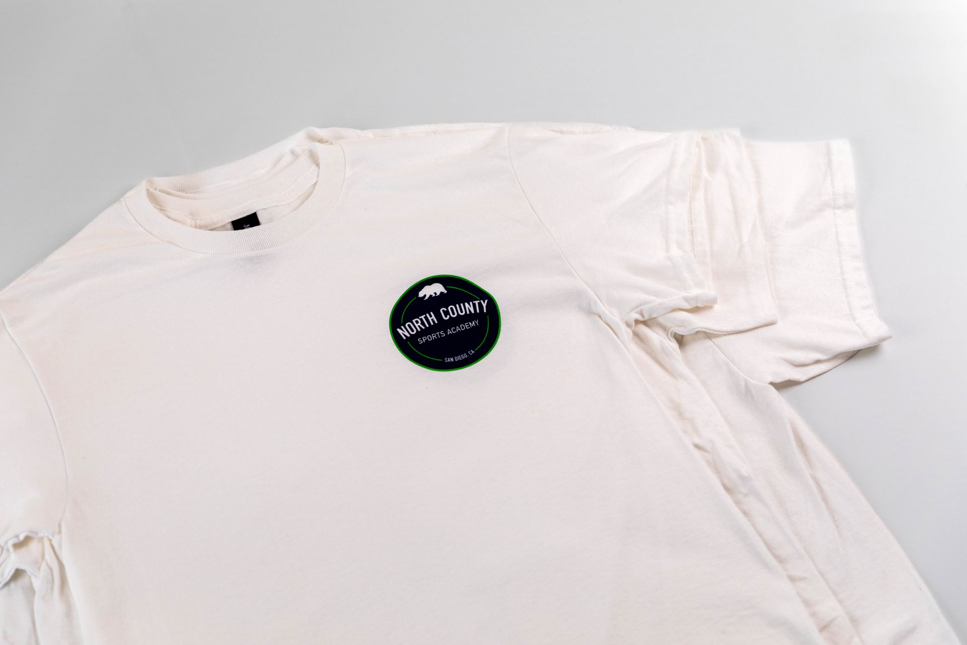 White T-shirt laid flat with a small circular logo on the chest
