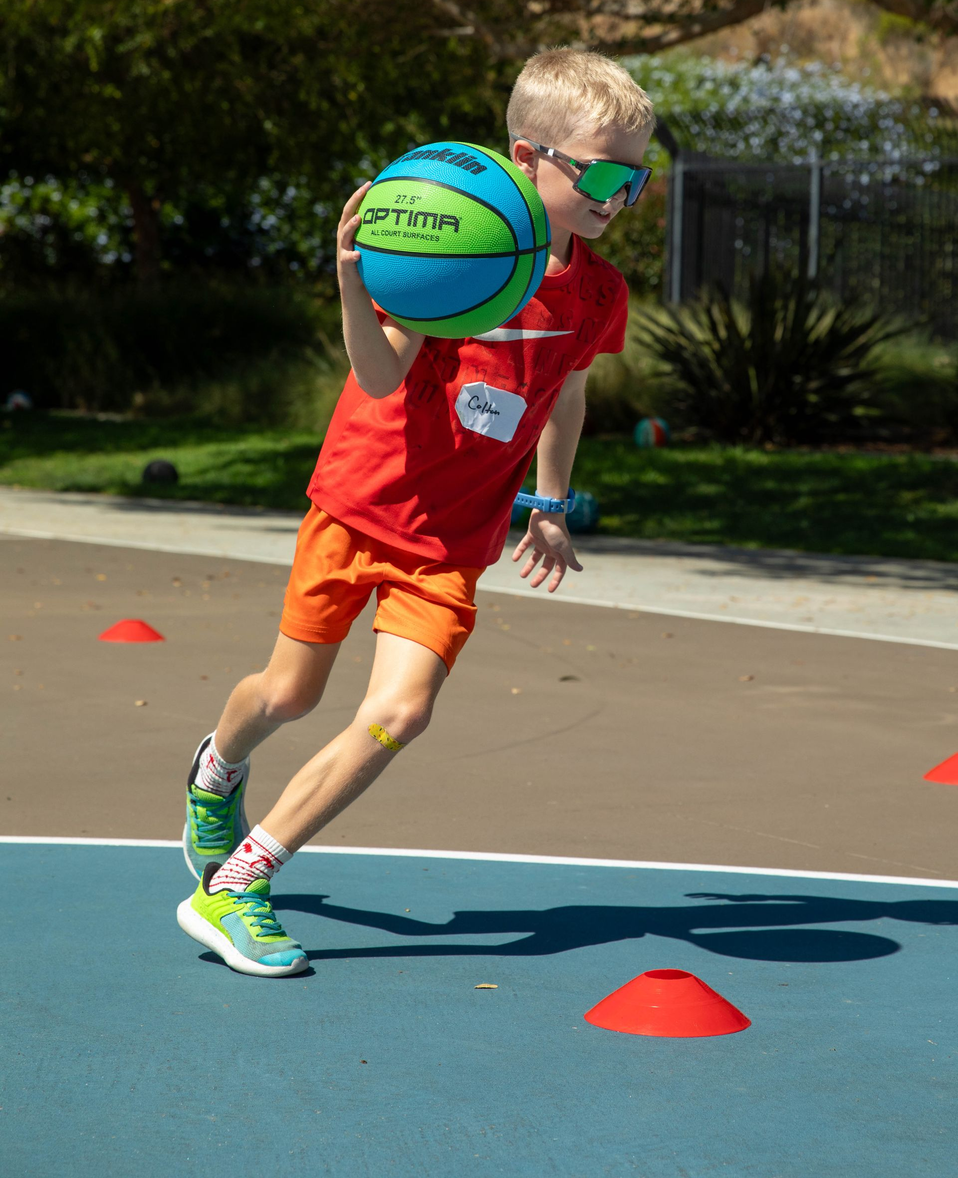 Children dribbling basketballs in a gym during practice, with a coach observing.