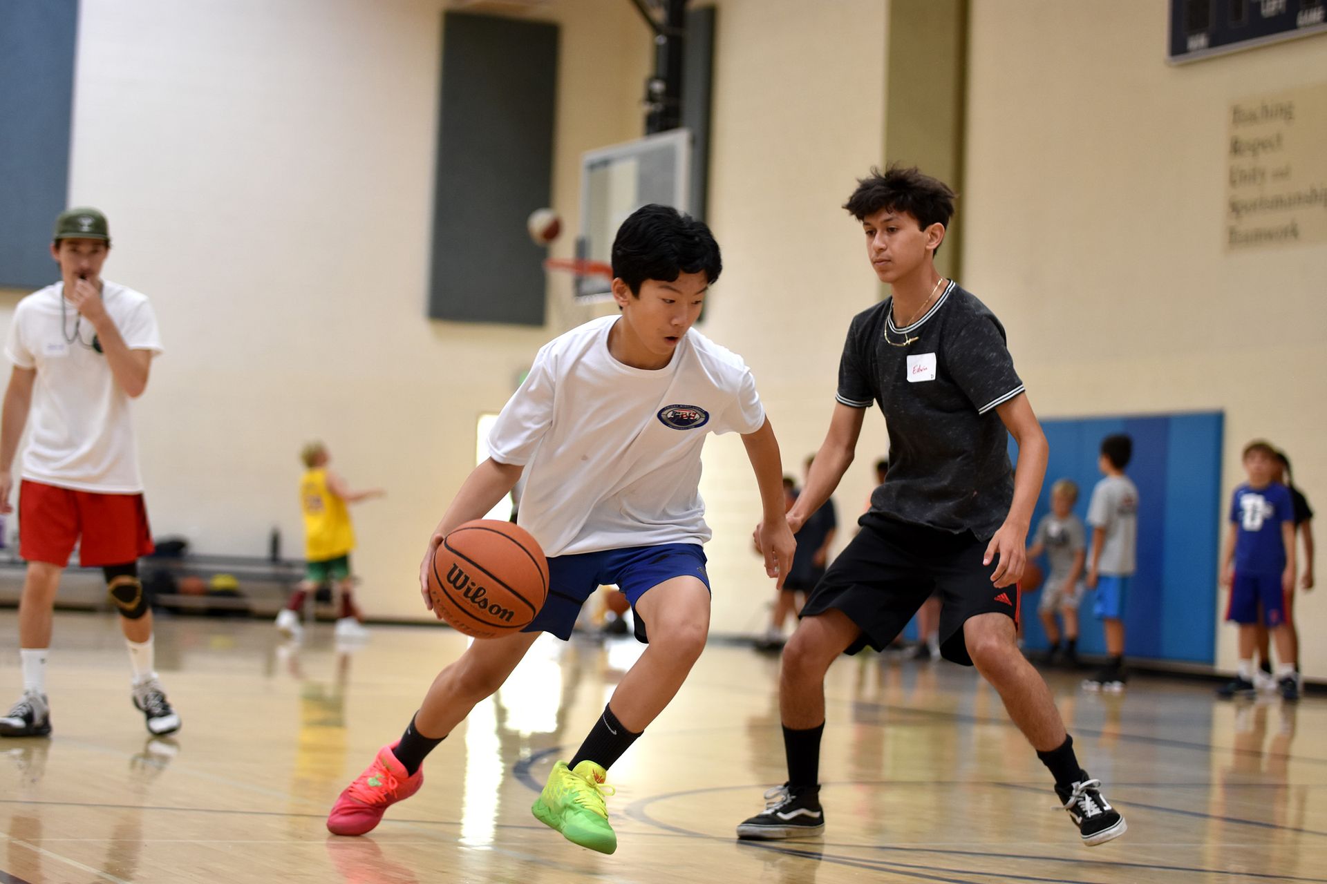 Basketball coach instructing children in a gym, with kids holding basketballs during practice