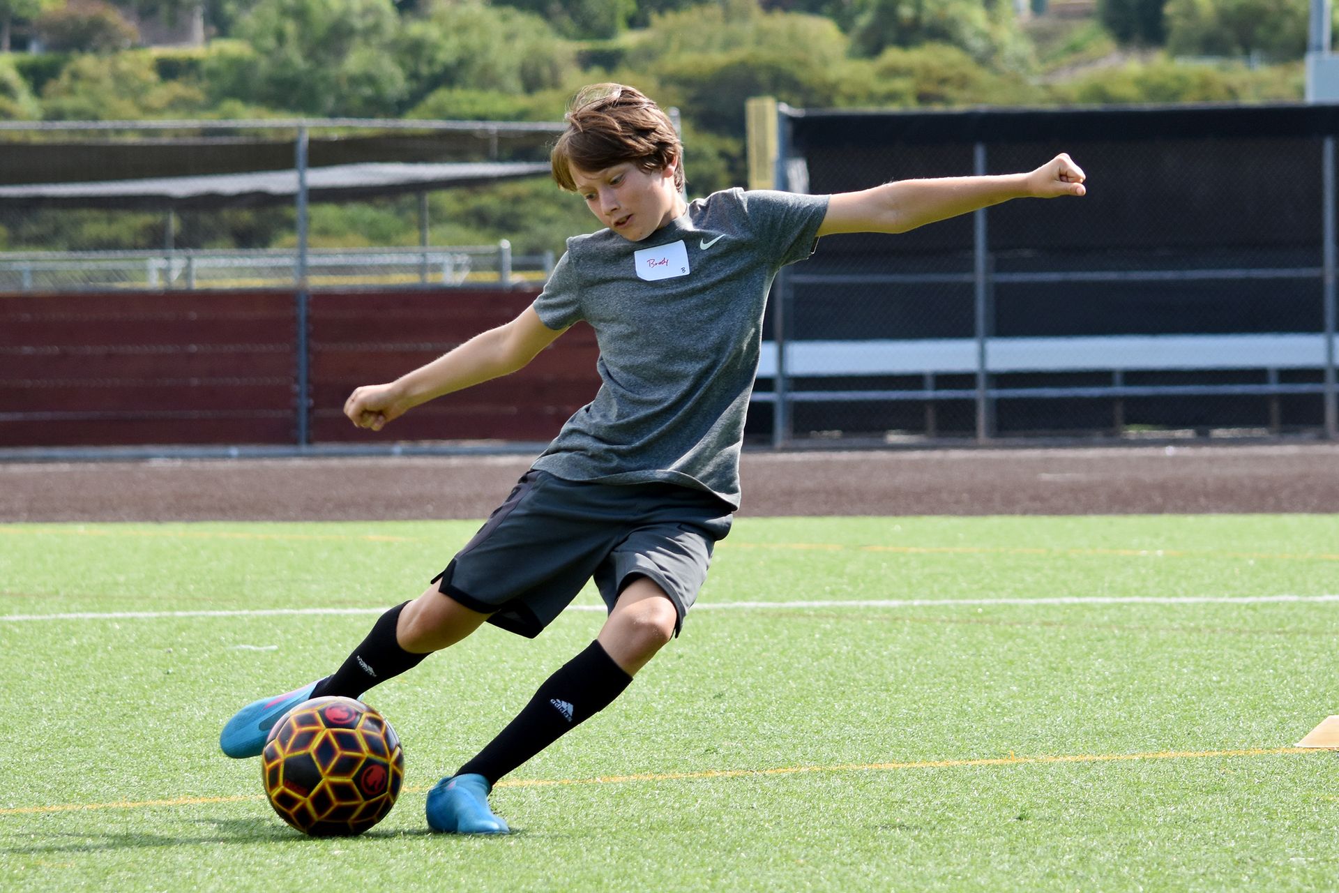 Soccer player in gray kit kicking a ball on a green field