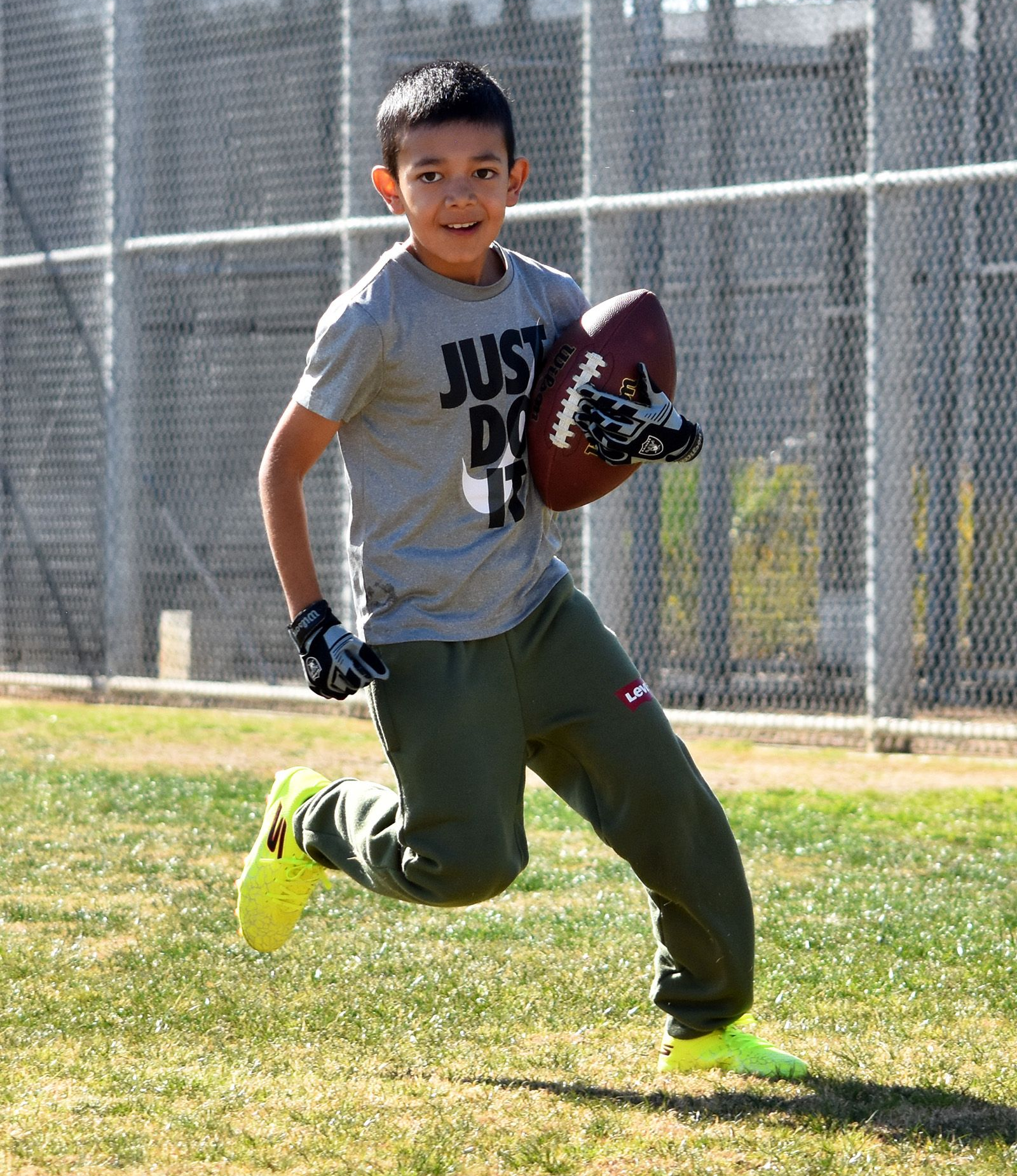 Children playing football on a grassy field, with one boy running forward holding the ball.