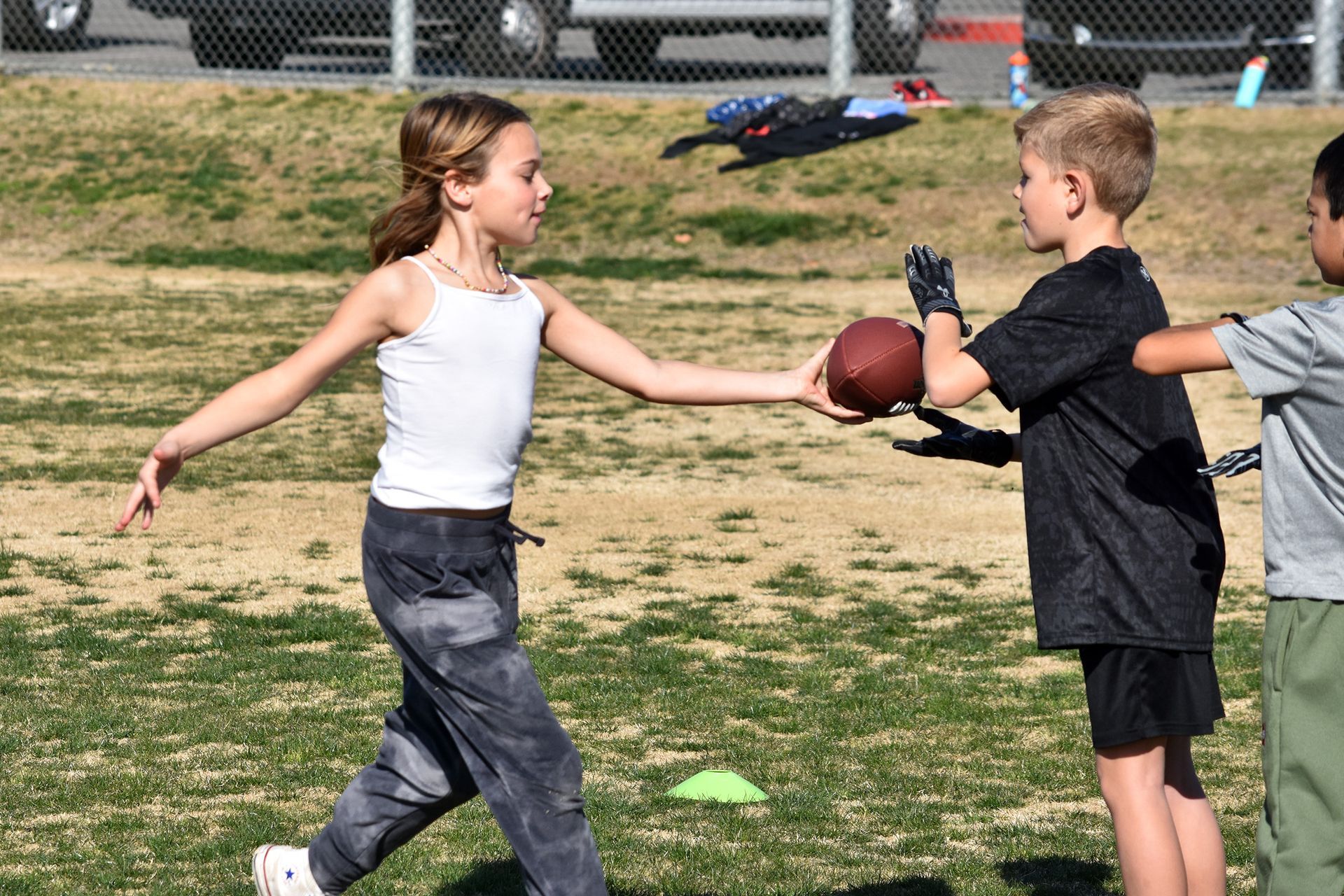 Two children pass a football on a grassy field during a casual outdoor game.