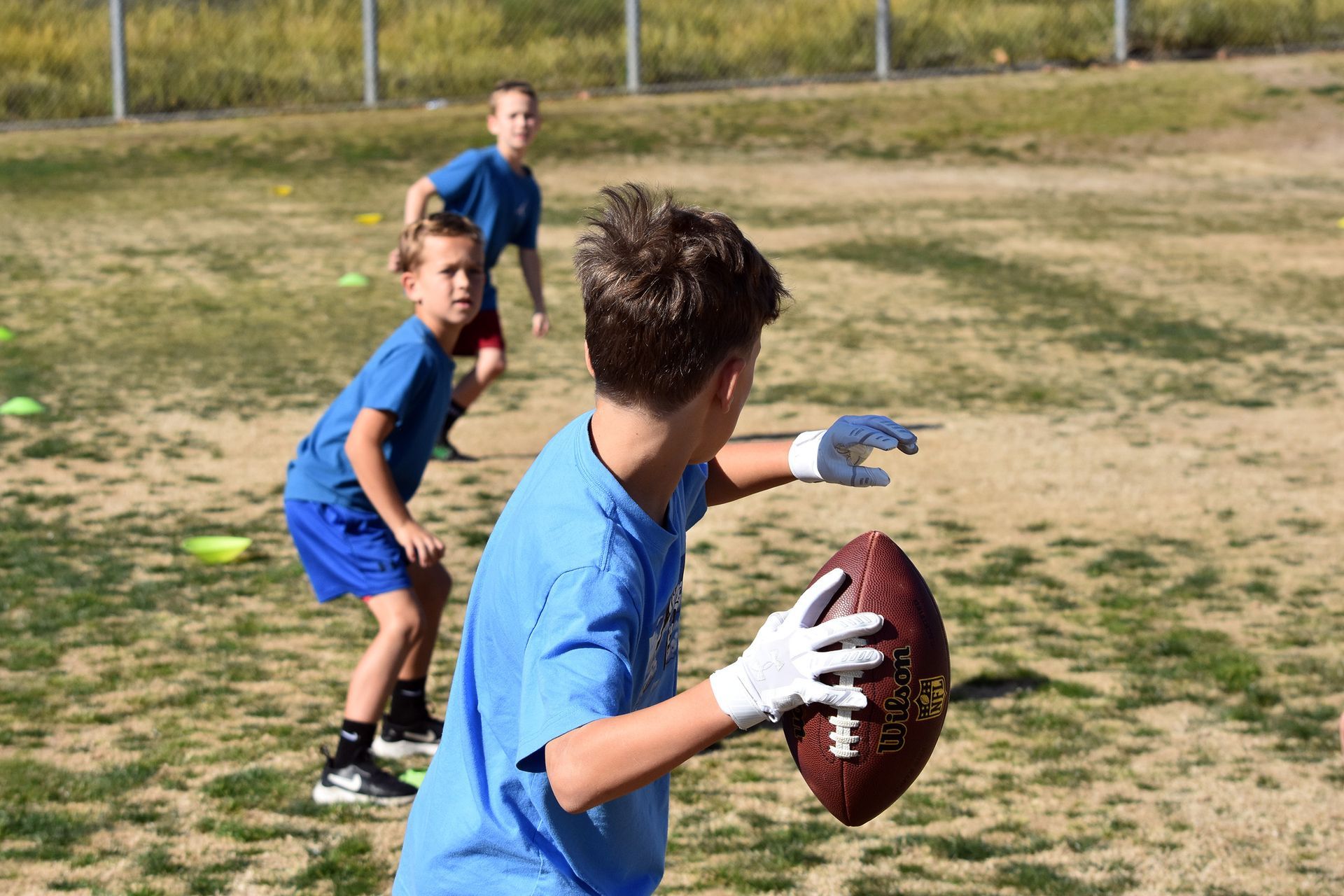 Kids in blue shirts playing catch with a football on a grassy field