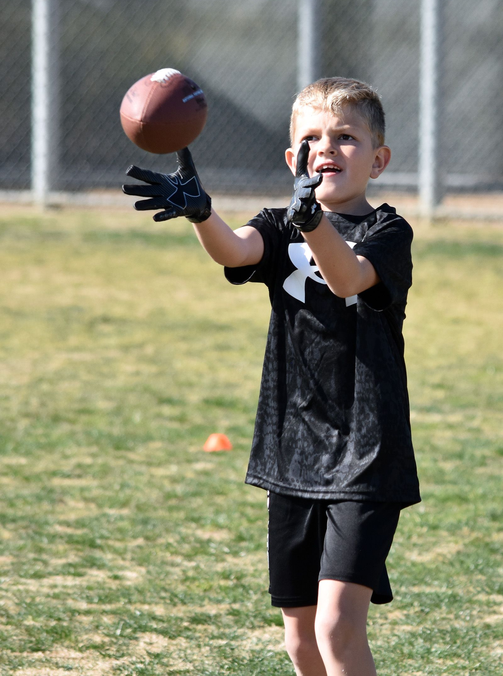 Boy reaching for a football during practice on a grassy field