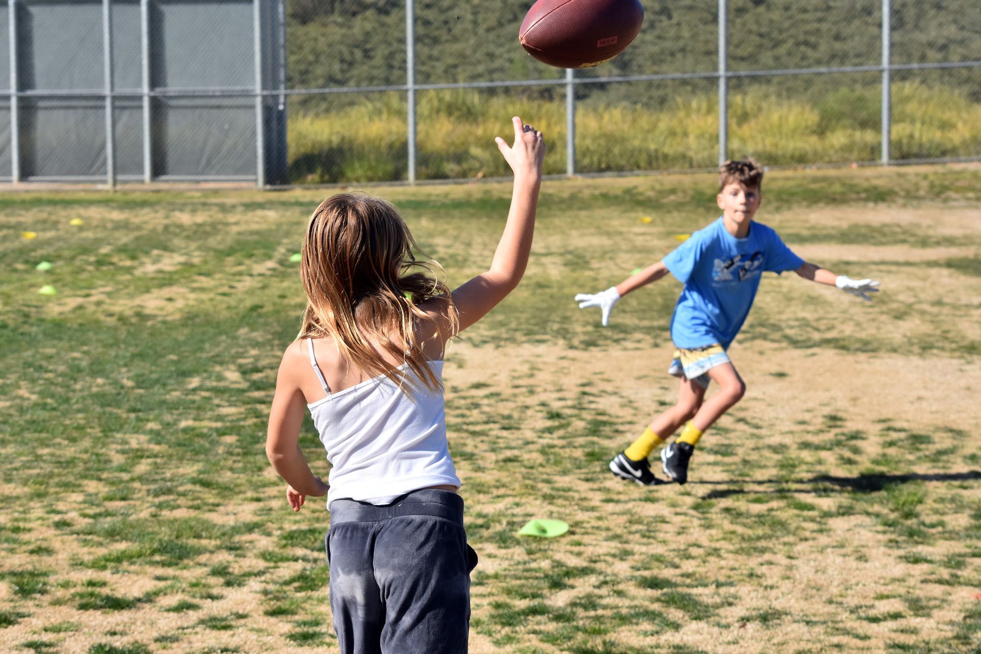 Two children playing catch on a grassy field, with one reaching for a football.