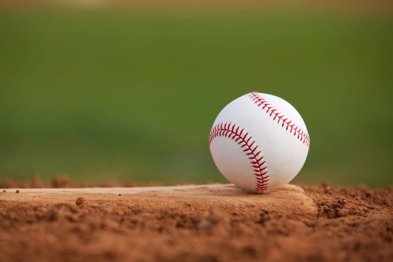 Baseball resting on dirt in a field, with a blurred green background