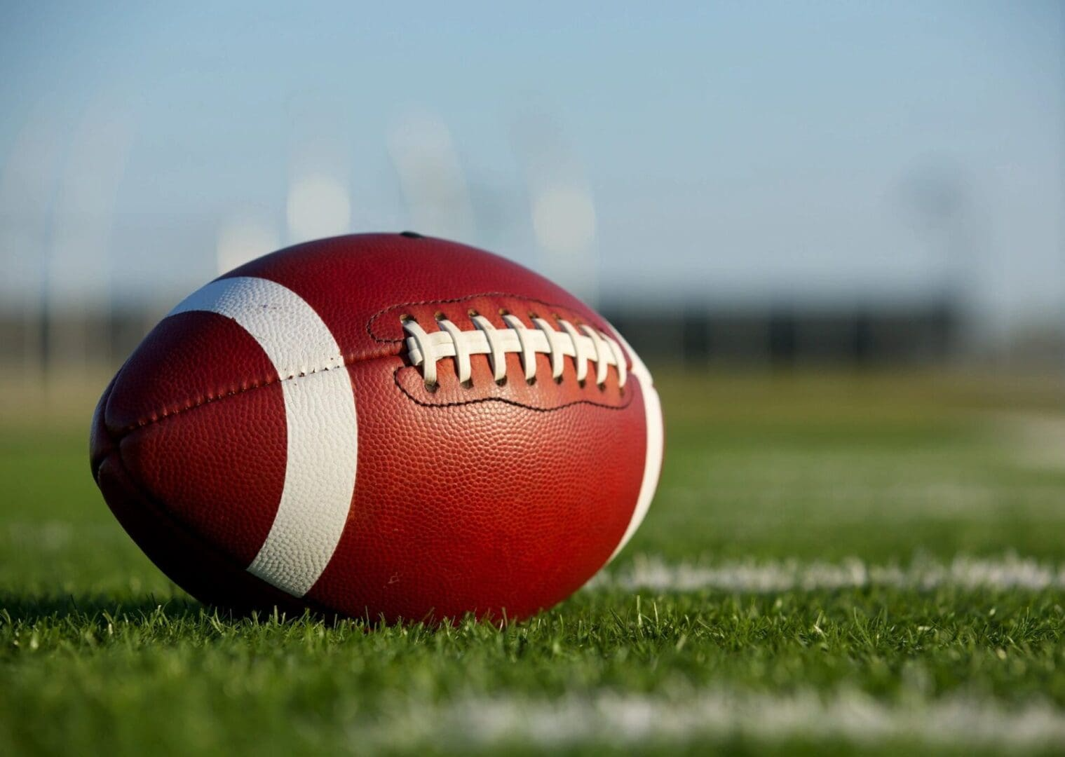 Brown football on green grass under a blue sky