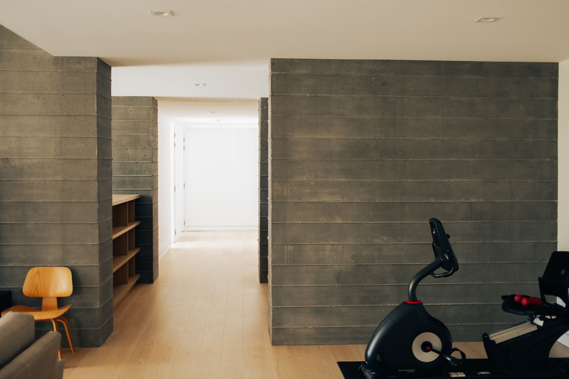 An exercise bike stands in front of a dark, horizontally paneled wall next to an open doorway and a wooden chair.