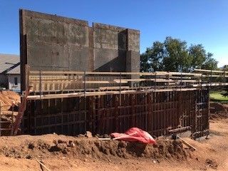 A construction site featuring a vertical concrete wall section and steel framework forms for future pouring.