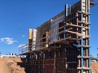 A tall, vertical concrete formwork structure stands at a construction site against a clear blue sky.