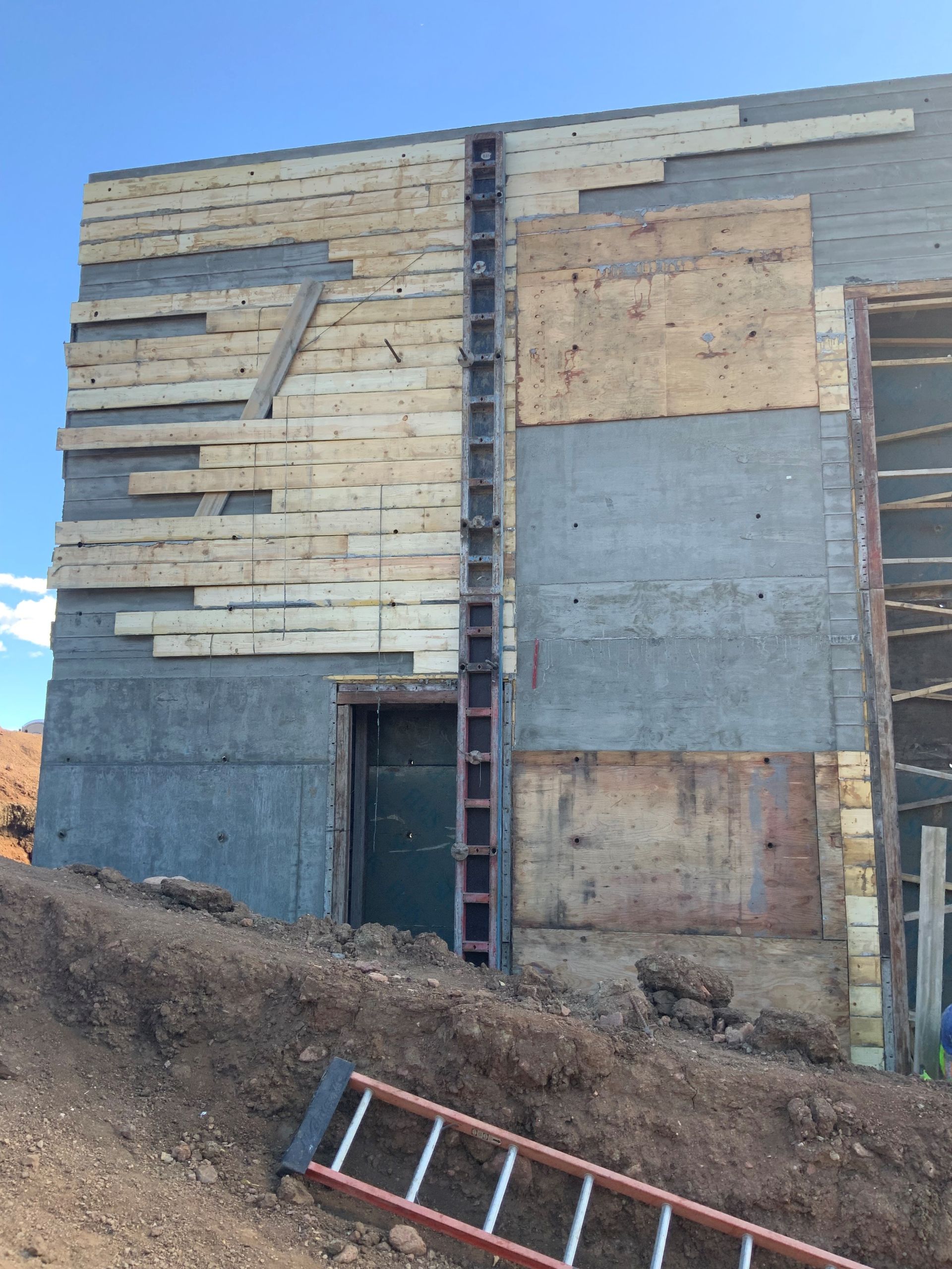 An unfinished concrete building wall with wood paneling and metal structural supports under a clear blue sky.