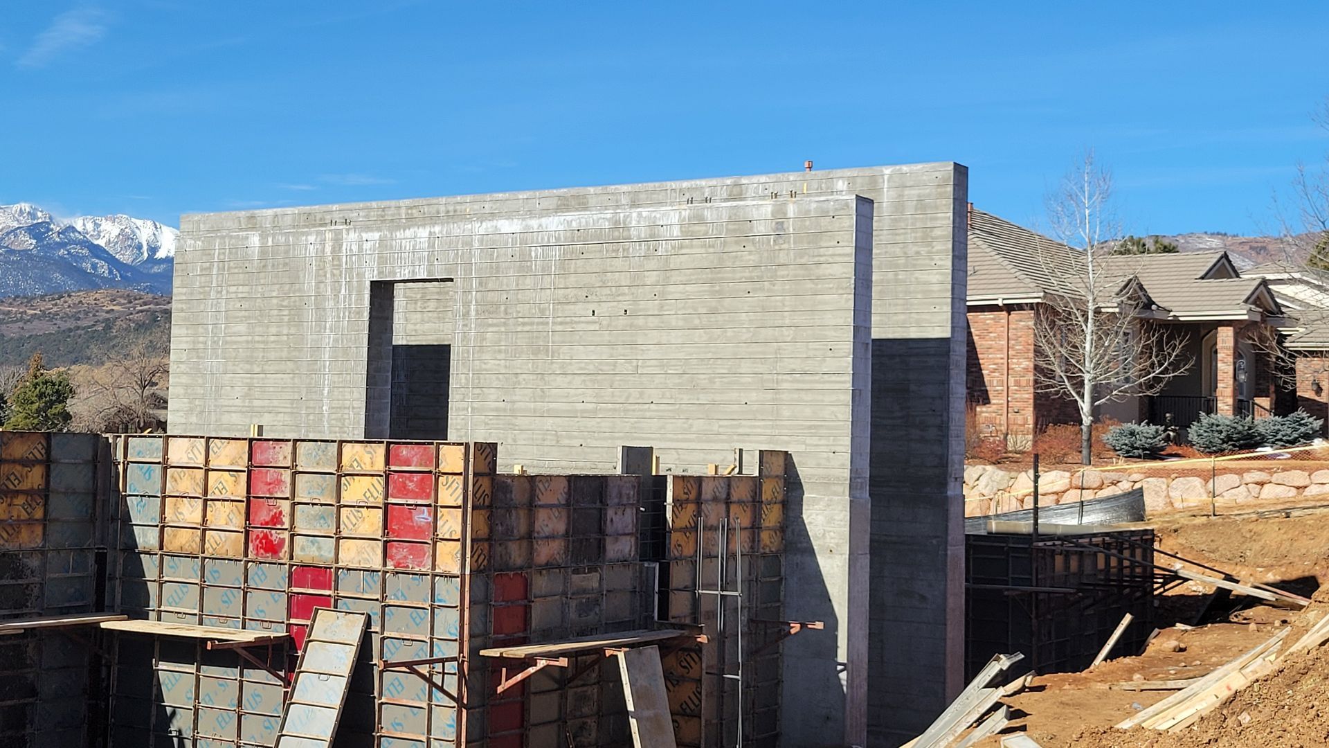 Concrete wall under construction with formwork panels against a blue sky and mountain backdrop.