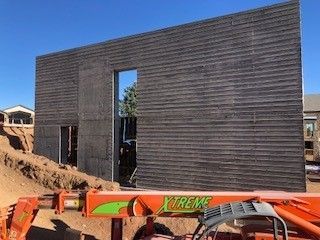 Large, unfinished concrete wall with horizontal textured finish and two large rectangular openings at a construction site.