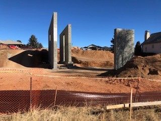 Three tall, gray concrete vertical panels standing in a construction site with piles of dirt under a clear blue sky.