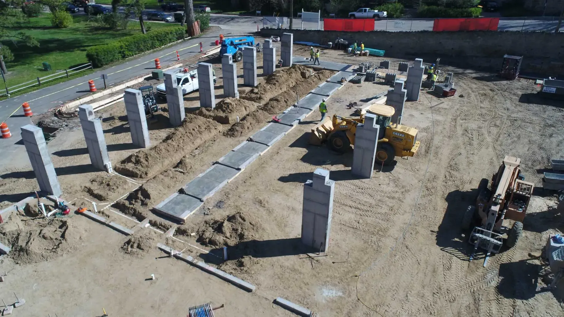 An aerial view of a construction site with several vertical concrete columns and a central trench lined with stone pavers.