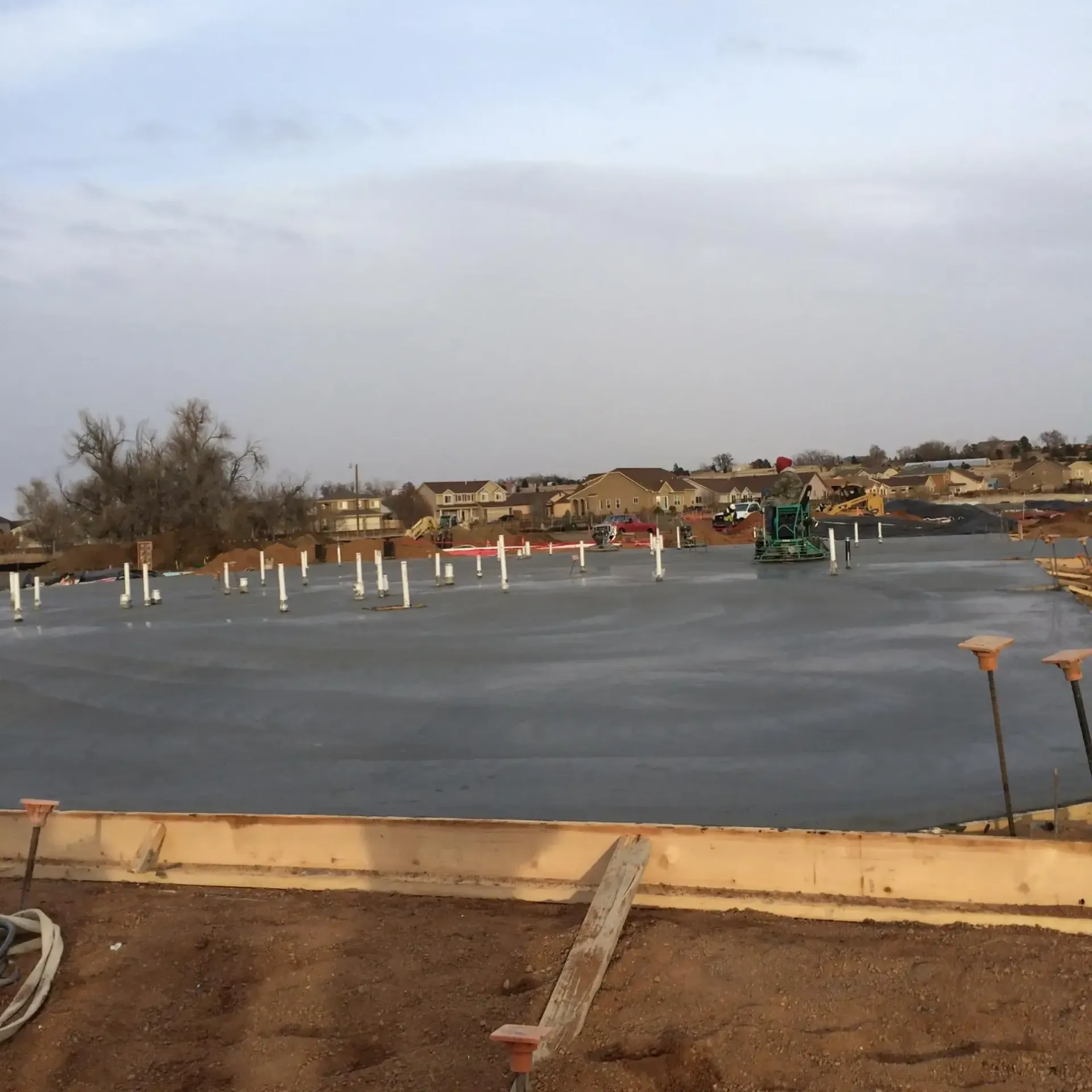 A concrete foundation slab at a construction site with protruding white pipes under a pale sky.