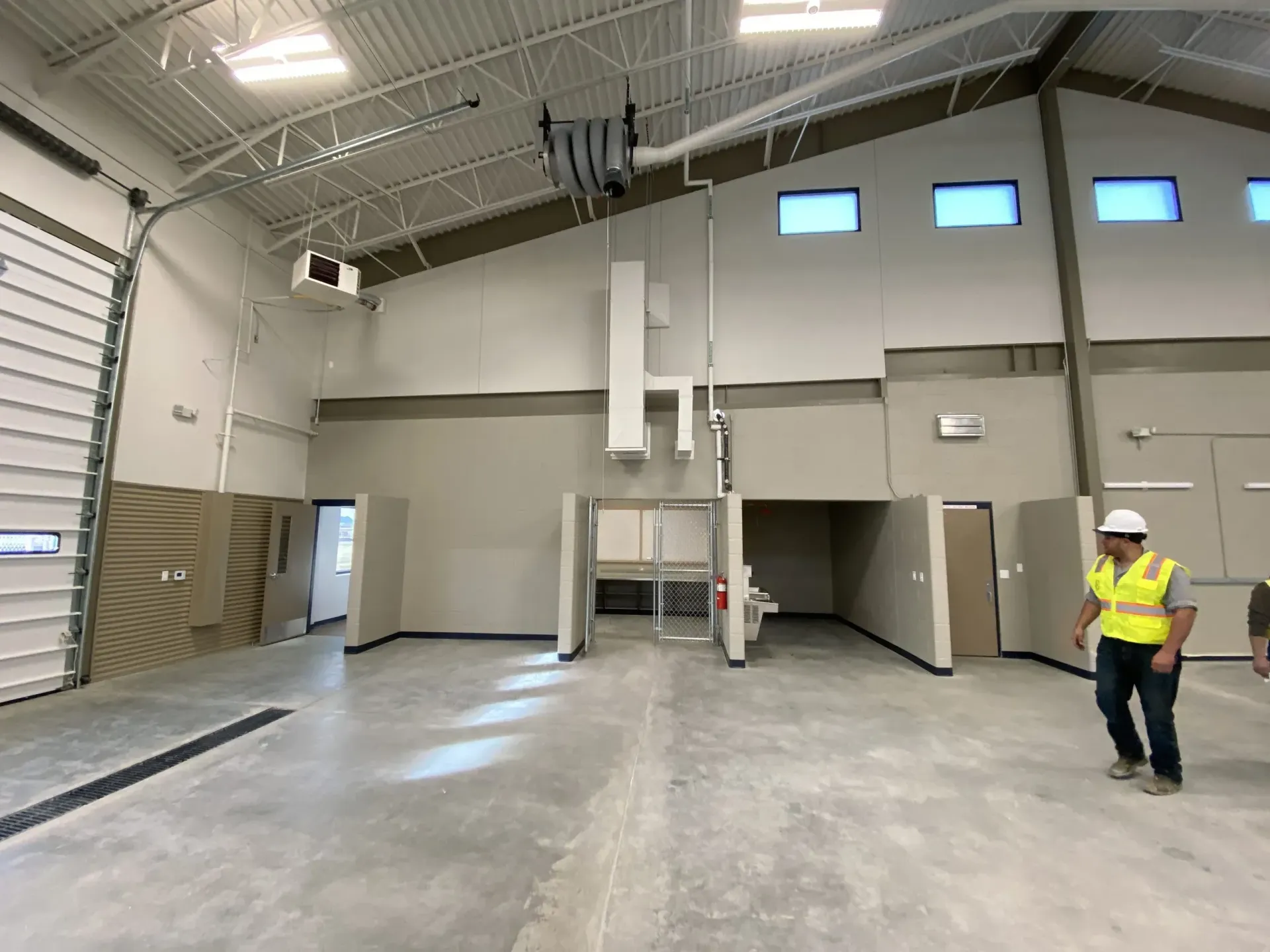 A construction worker in a high-visibility vest stands in an unfinished, high-ceilinged industrial building.