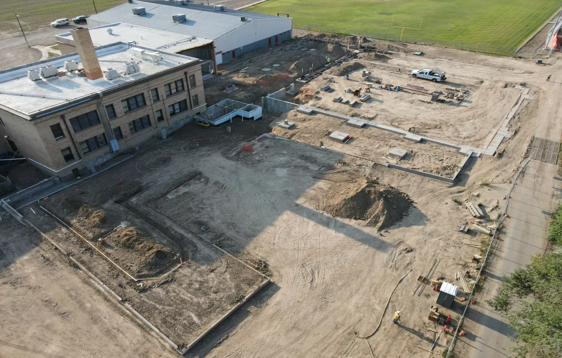 Aerial view of a construction site showing foundation trenches and excavated dirt next to a brick building.