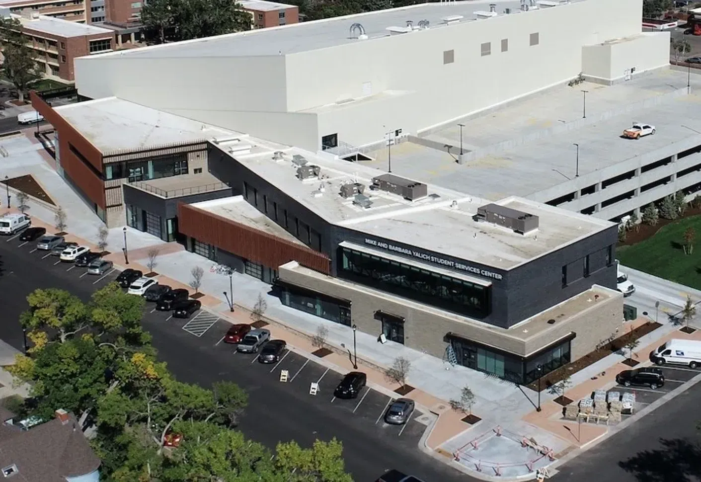Aerial view of a multi-level modern commercial building with a tan and dark grey exterior, adjacent to a large parking lot.
