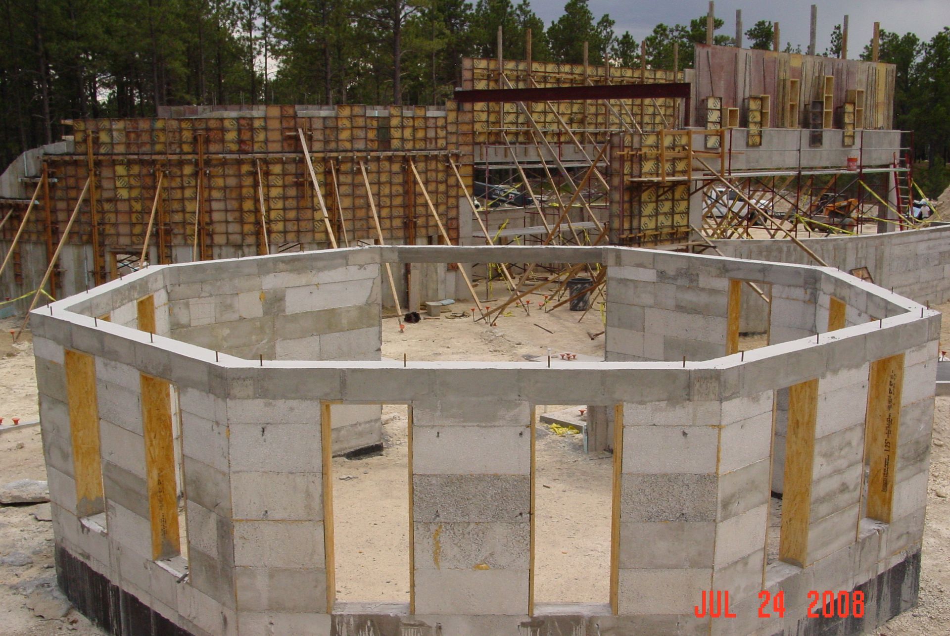 An octagonal concrete block foundation under construction with wooden formwork and steel framing visible in the background.