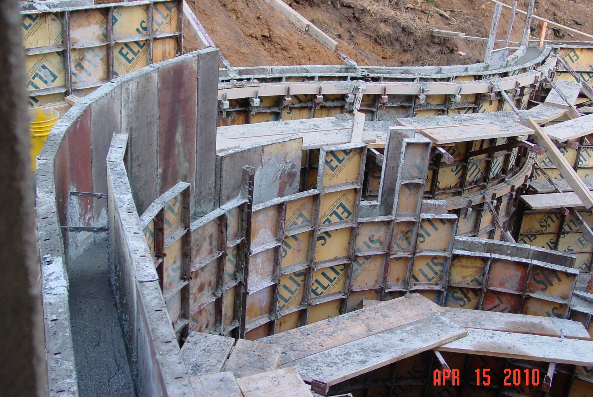 Construction site showing curved concrete formwork panels being installed for a foundation wall, dated April 15, 2010.