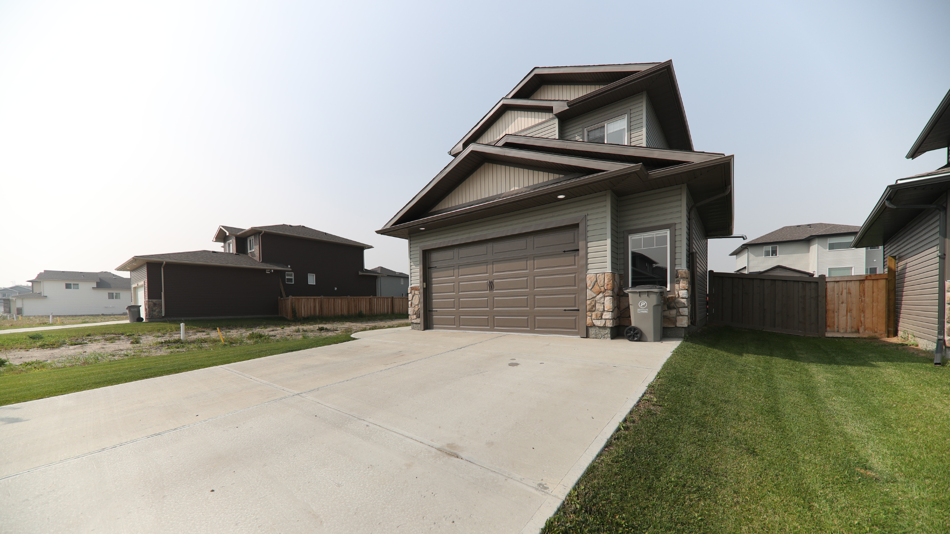 A modern two-story home with a brown garage and stone facade, fronted by a concrete driveway and green lawn.