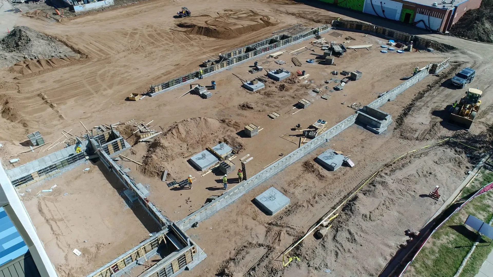 Aerial view of a construction site showing concrete foundations, excavated trenches, and scattered building materials.