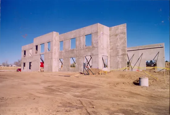 Concrete panels for a building structure under construction on a dirt lot against a clear blue sky.