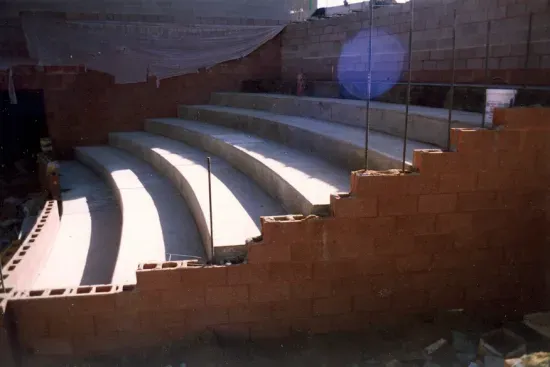 Construction of curved concrete stadium-style tiered seating within a brick-walled outdoor area.