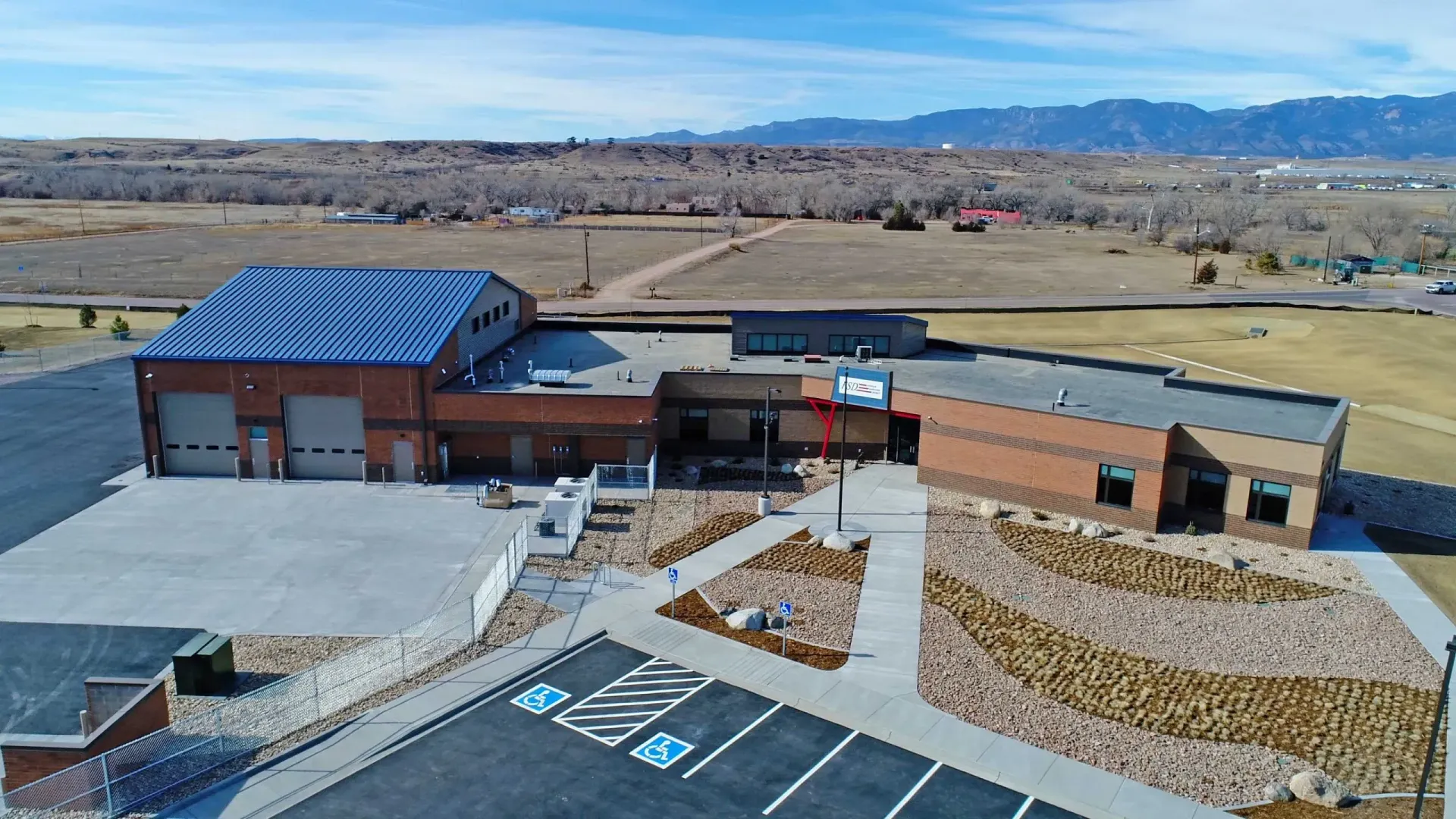 Aerial view of a brick fire station with solar panels on the roof, surrounded by a paved lot and a dry, open landscape.