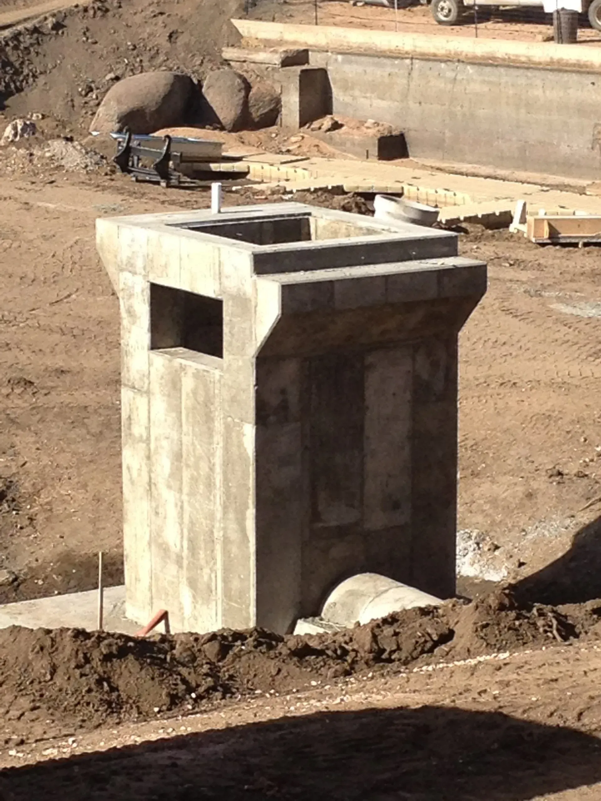 A precast concrete storm drain inlet structure stands on a dirt construction site.