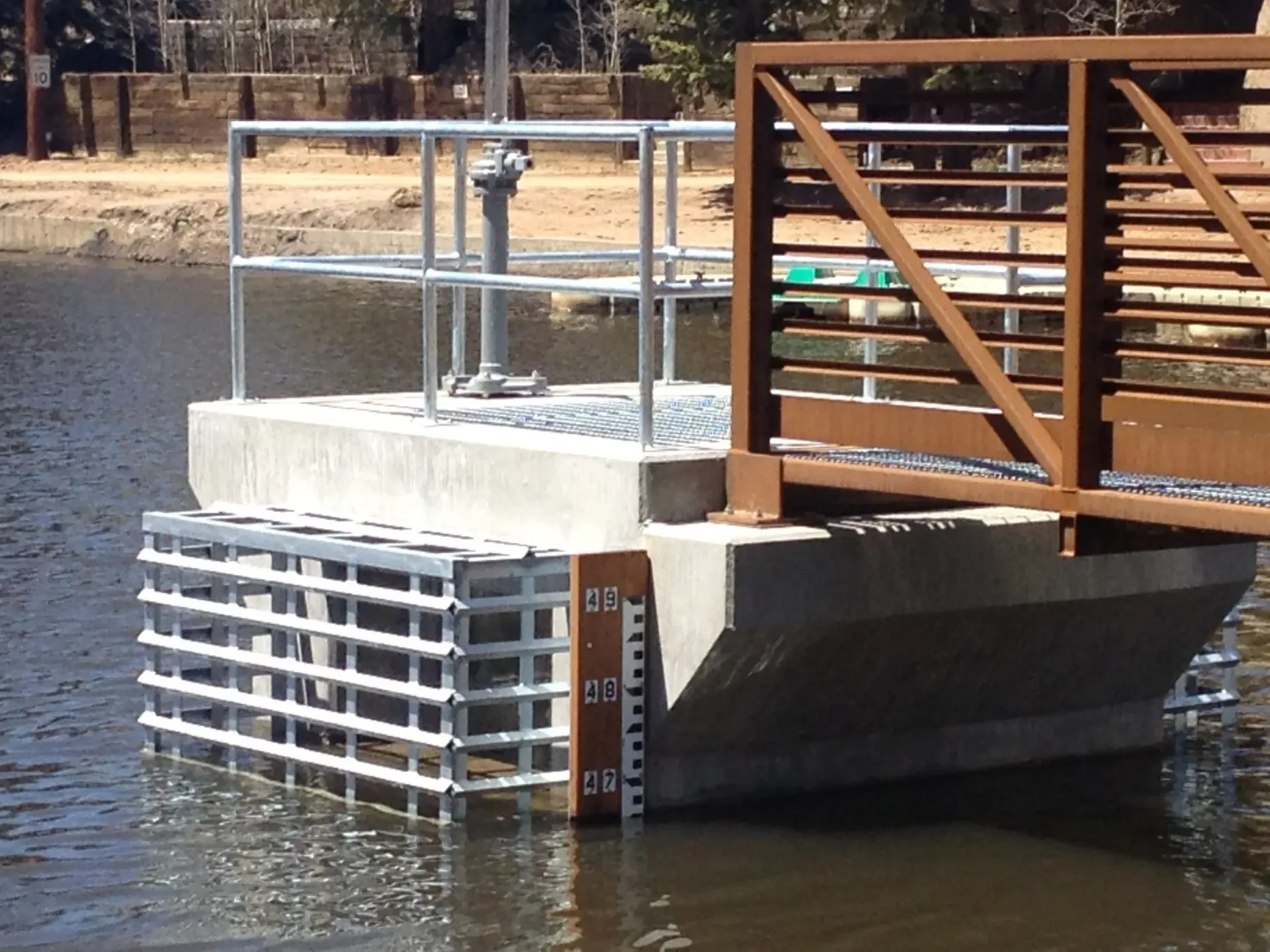 A concrete water intake structure with a metal grate and bridge extending over a lake, featuring a water depth gauge.